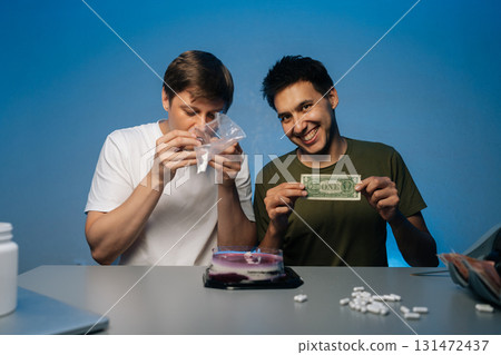 Portrait of cheerful young men sitting at table with cake and cash, preparing drugs from plastic bag while getting ready to celebrate birthday party filled with excitement and risk. Portrait of cheerful young men sitting at table with cake and cash, preparing drugs from plastic bag while getting ready to celebrate birthday party filled with excitement and risk. 131472437