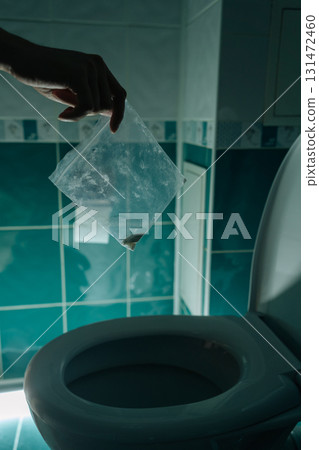 Vertical cropped shot of male hand holding plastic bag with drugs over open toilet, ready to dispose of illegal substance in dark bathroom, representing drug abuse, disposal and dealing with addiction Vertical cropped shot of male hand holding plastic bag with drugs over open toilet, ready to dispose of illegal substance in dark bathroom, representing drug abuse, disposal and dealing with addiction 131472460