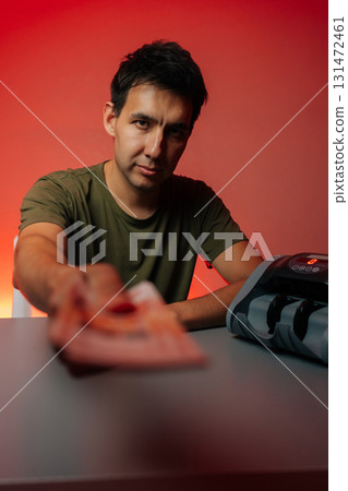 Cashier handing out banknotes looking at camera while positioned next to money counting machine on table, set against vibrant red background, captures moment of financial transaction. Cashier handing out banknotes looking at camera while positioned next to money counting machine on table, set against vibrant red background, captures moment of financial transaction. 131472461