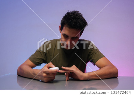 Portrait of young man sitting at a table, using electric nail clipper for personal manicure. Vibrant colors in background enhance modern, stylish atmosphere of self-care and grooming. Portrait of young man sitting at a table, using electric nail clipper for personal manicure. Vibrant colors in background enhance modern, stylish atmosphere of self-care and grooming. 131472464