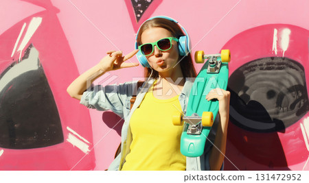 Stylish modern young teenager girl with skateboard in glasses, listening to music, graffiti wall Stylish modern young teenager girl with skateboard in glasses, listening to music, graffiti wall 131472952