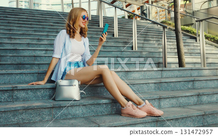 Stylish modern happy smiling young woman with phone in city park, girl holding smartphone on street Stylish modern happy smiling young woman with phone in city park, girl holding smartphone on street 131472957