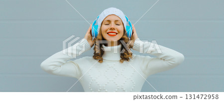 Portrait happy inspired young woman enjoying listening to music in headphones in white hat, sweater Portrait happy inspired young woman enjoying listening to music in headphones in white hat, sweater 131472958