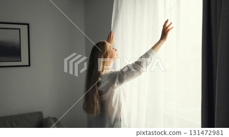 Woman opening window curtains at home in morning Woman opening window curtains at home in morning 131472981