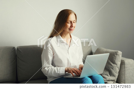 Happy modern woman working with laptop, freelancer girl sitting on a couch in the living room Happy modern woman working with laptop, freelancer girl sitting on a couch in the living room 131472983