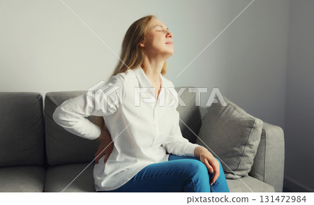Woman suffering from back pain while sitting on couch at home Woman suffering from back pain while sitting on couch at home 131472984