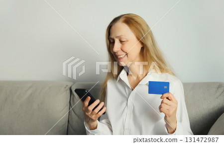 Woman holding plastic credit bank card, looking at phone, shopping online or ordering goods at home 131472987