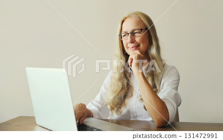 Happy woman working with laptop sitting at desk in office or at home Happy woman working with laptop sitting at desk in office or at home 131472991