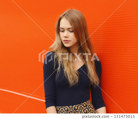 Beautiful young woman model with long blonde hair standing against a red background 131473013