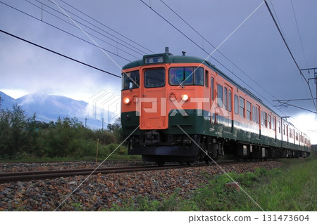 Shinano Railway 115 series train (Shonan color) running through Karuizawa on a cloudy day, watched over by Mount Asama. Photo taken on September 27, 2025. 131473604