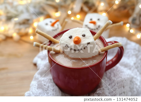 Marshmallow snowman with carrot nose floating in cup of hot chocolate, cappuccino, chocolate drink, with candy canes, Christmas background, bokeh lights in the background 131474052