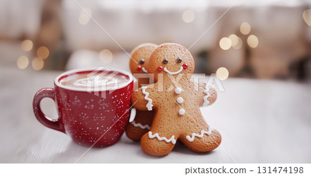 Gingerbread man cookie leaning on red coffee cup in warm Christmas setting tree lights background 131474198