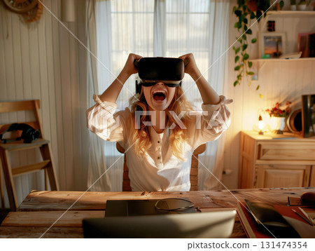 Young woman cheering while wearing VR headset in cozy room with gaming setup and warm lighting Young woman cheering while wearing VR headset in cozy room with gaming setup and warm lighting 131474354