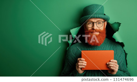 Surprised red-haired middle-aged man with big red box his hands looks through torn hole green paper background, red beard, celebration St. Patrick's Day Surprised red-haired middle-aged man with big red box his hands looks through torn hole green paper background, red beard, celebration St. Patrick's Day 131474696