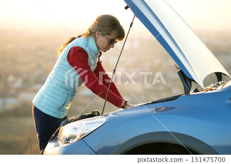 Young woman standing near broken down car with popped up hood having trouble with her vehicle. 131475700