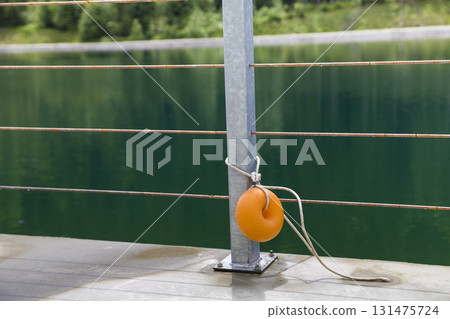 Yellow plastic buoy attached to a metal fence on the bank of a lake with green water. Yellow plastic buoy attached to a metal fence on the bank of a lake with green water. 131475724
