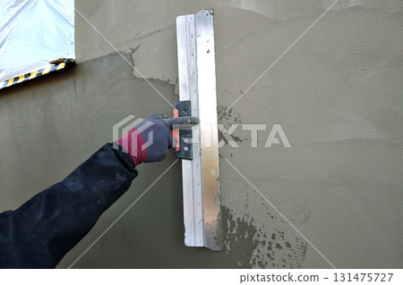 Worker covering insulated wall with solution of glue over plastered styrofoam insulation. Worker covering insulated wall with solution of glue over plastered styrofoam insulation. 131475727