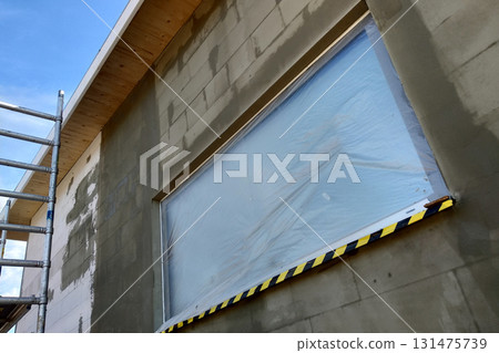 Window of a house under construction covered with protective plastic film. 131475739