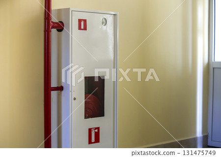 White metal cabinet with fire extinguishing hose reel on light wall copy space background. 131475749