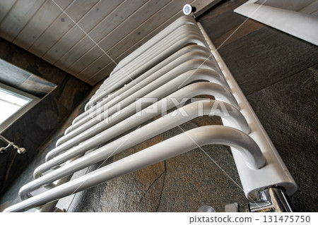 White contemporary electric towel dryer mounted on black tiled wall in modern bathroom. 131475750