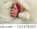 Soft feet of a new born in a white wool blanket. Close up of toes, heels and feet of a newborn. Knitted white heart in the legs of a baby. Macro photography.The tiny foot of a newborn baby 131476003