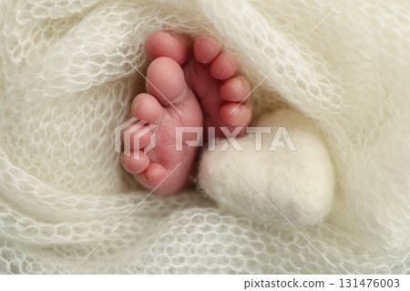 Soft feet of a new born in a white wool blanket. Close up of toes, heels and feet of a newborn. Knitted white heart in the legs of a baby. Macro photography.The tiny foot of a newborn baby Soft feet of a new born in a white wool blanket. Close up of toes, heels and feet of a newborn. Knitted white heart in the legs of a baby. Macro photography.The tiny foot of a newborn baby 131476003