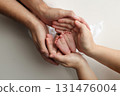 A father and mother hold the feet of a newborn child in a white blanket on a white background.. The feet of a newborn in the hands of parents. Photo of foot, heels and toes.The palms of the parents. 131476004