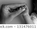 Close-up little hand of child and palm of mother and father. The newborn baby has a firm grip on the parent's finger after birth. A newborn holds on to mom's, dad's finger. Black and white photo. 131476011