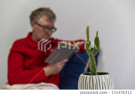elderly person reading book with cactus plant in cozy indoor setting. selective focus. closeup. elderly person reading book with cactus plant in cozy indoor setting. selective focus. closeup. 131476312