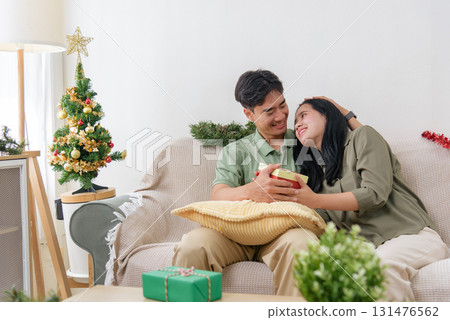Christmas celebration brings happy couple loving winter holiday joy, man gives gift to woman in cozy home, decorated tree creates festive christmas atmosphere, warm interior. Christmas celebration brings happy couple loving winter holiday joy, man gives gift to woman in cozy home, decorated tree creates festive christmas atmosphere, warm interior. 131476562