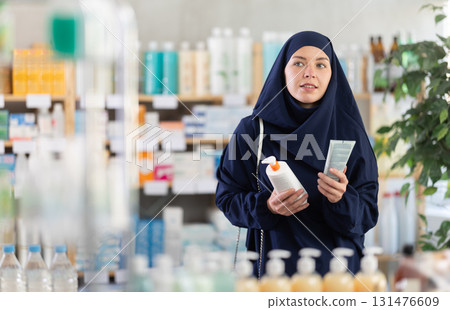 Young woman in khimar choosing facial cream in pharmacy Young woman in khimar choosing facial cream in pharmacy 131476609