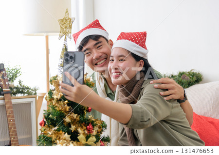 Christmas happy couple shares love, smiling taking selfie photograph, wearing Santa hats at home, celebrating winter holiday spirit, enjoying festive christmas celebration with joyful embrace. Christmas happy couple shares love, smiling taking selfie photograph, wearing Santa hats at home, celebrating winter holiday spirit, enjoying festive christmas celebration with joyful embrace. 131476653