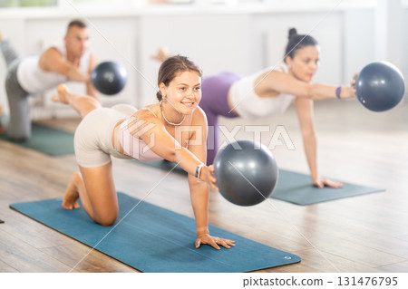 Men and woman diligently perform set of exercises with fitball during training session 131476795
