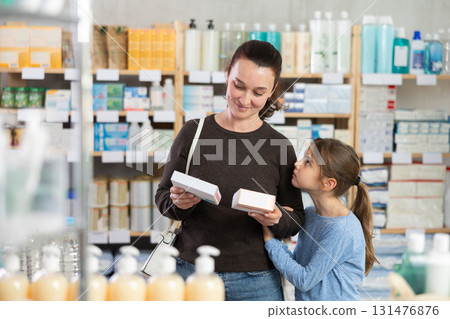 Woman with schoolgirl daughter are busy choosing tablet box at pharmacy Woman with schoolgirl daughter are busy choosing tablet box at pharmacy 131476876