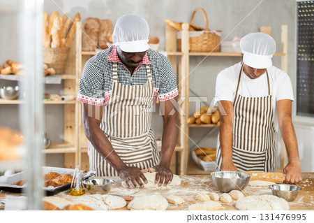 Two male bakers kneading dough and rolling it out 131476995