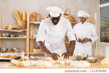 African man works as baker in bakery, molds pies from dough, creates croissants from dough African man works as baker in bakery, molds pies from dough, creates croissants from dough 131476999
