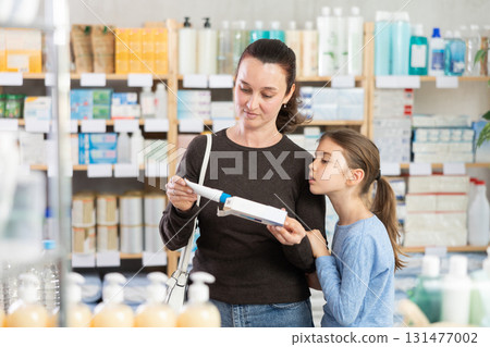 woman and her daughter choose an ointment at a pharmacy near the counter woman and her daughter choose an ointment at a pharmacy near the counter 131477002