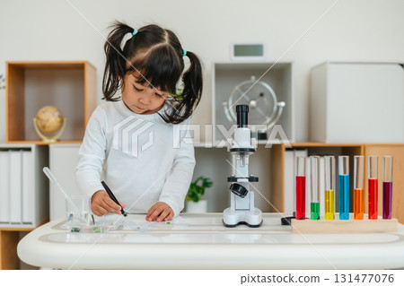 toddler girl scientist using tongs putting herbal sample in slide, preparing specimen for science microscope 131477076