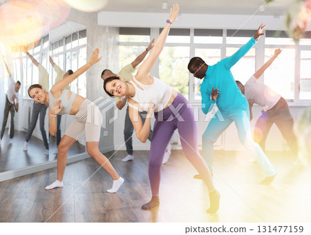 Pretty girl and multinational group of active young people practicing rock and roll dance in dance hall 131477159