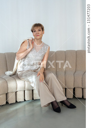 Smiling woman sitting on sofa in bright sunny room. Looking at camera. Vertical photo. High quality photo 131477203