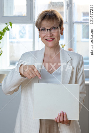 Portrait of emotional woman. Confident woman showing direction with hand on white sheet of paper with space for tex. Looking at camera, banner. Vertical photo. High quality photo Portrait of emotional woman. Confident woman showing direction with hand on white sheet of paper with space for tex. Looking at camera, banner. Vertical photo. High quality photo 131477235