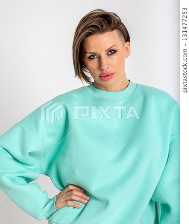 Portrait beautiful woman of model appearance. Girl in mint jumper, black trousers on grey background. Pretty female with trendy makeup posing in studio. Vertical photo. 131477253