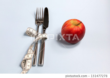 Fork and knife wrapped in a measuring tape and a red apple nearby 131477278