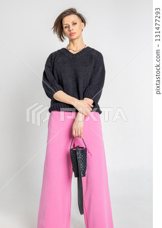 Portrait beautiful woman of model appearance. Girl in black jumper and pink trousers on grey background. Pretty female with trendy makeup posing in studio. Vertical photo. Portrait beautiful woman of model appearance. Girl in black jumper and pink trousers on grey background. Pretty female with trendy makeup posing in studio. Vertical photo. 131477293