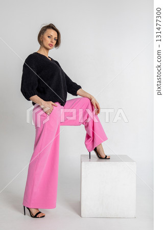 Portrait beautiful woman of model appearance. Girl in black jumper and pink trousers on grey background. Pretty female with trendy makeup posing in studio. Vertical photo.  131477300