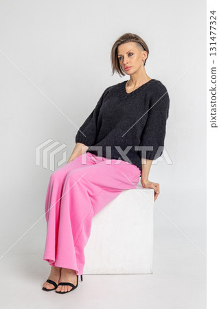 Portrait beautiful woman of model appearance. Girl in black jumper and pink trousers on grey background. Pretty female with trendy makeup posing in studio. Vertical photo. Portrait beautiful woman of model appearance. Girl in black jumper and pink trousers on grey background. Pretty female with trendy makeup posing in studio. Vertical photo. 131477324