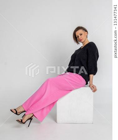 Portrait beautiful woman of model appearance. Girl in black jumper and pink trousers on grey background. Pretty female with trendy makeup posing in studio. Vertical photo.  131477341