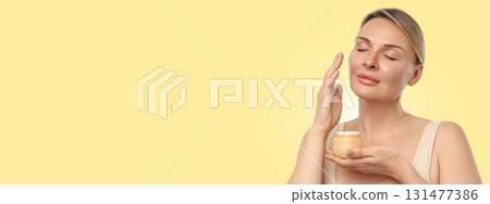 Female applying moisturizer while holding a cream container Female applying moisturizer while holding a cream container 131477386