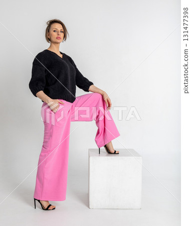 Portrait beautiful woman of model appearance. Girl in black jumper and pink trousers on grey background. Pretty female with trendy makeup posing in studio. Vertical photo. Portrait beautiful woman of model appearance. Girl in black jumper and pink trousers on grey background. Pretty female with trendy makeup posing in studio. Vertical photo. 131477398