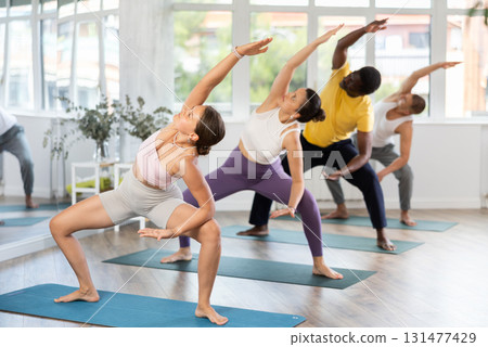 Young woman coach and students perform utkata konasana during training in studio Young woman coach and students perform utkata konasana during training in studio 131477429